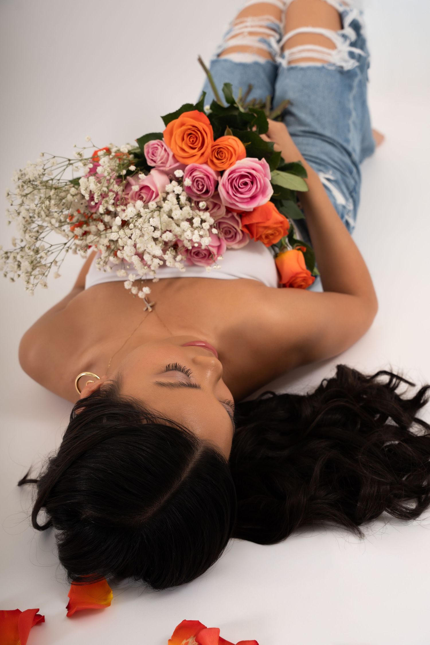 A women poses with a bouquet of flowers on a white backdrop laying down.