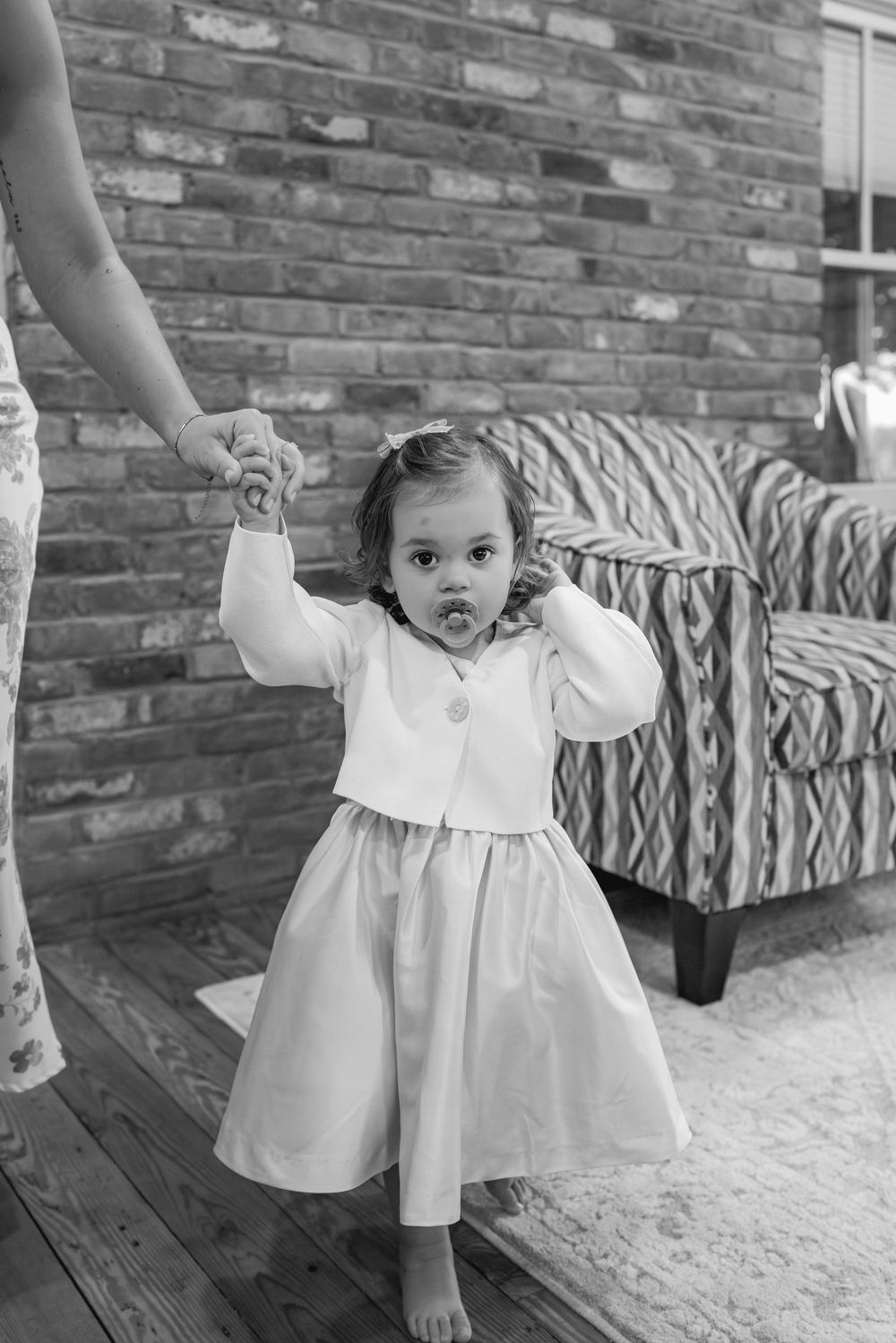 A small child in a white dress plays energetically on a porch with a brick wall background.