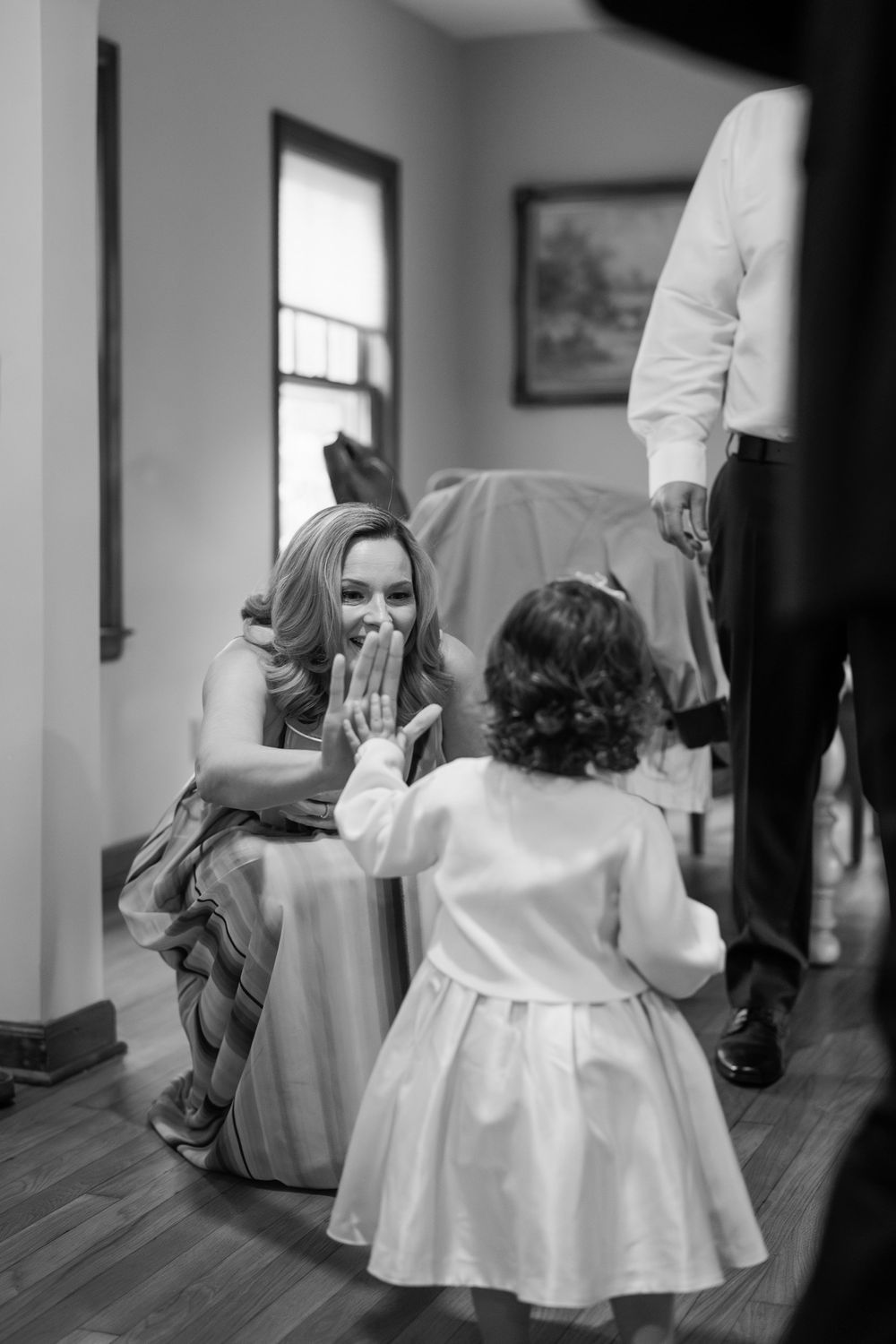 A heartwarming black and white moment between a woman in a dress and a small child giving each other a high five.