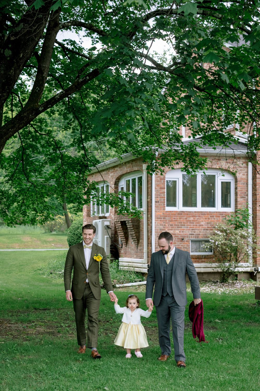 A group walking together on a lush green lawn beside a brick building in formal attire.