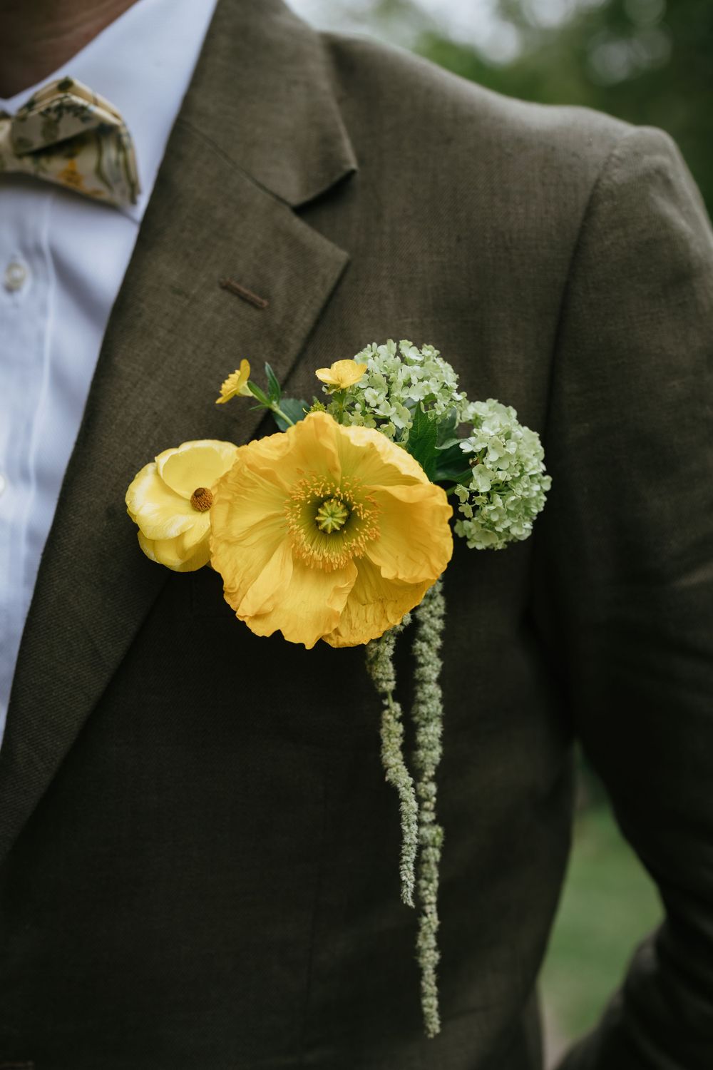 A yellow poppy boutonniere with green amaranthus on a brown suit lapel shown from different angles.