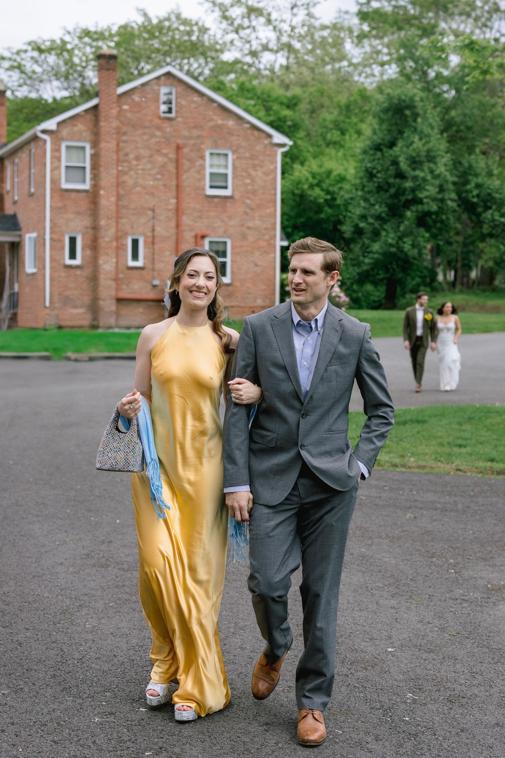 A couple walking together outdoors, with one wearing a yellow dress and the other in a dark suit.