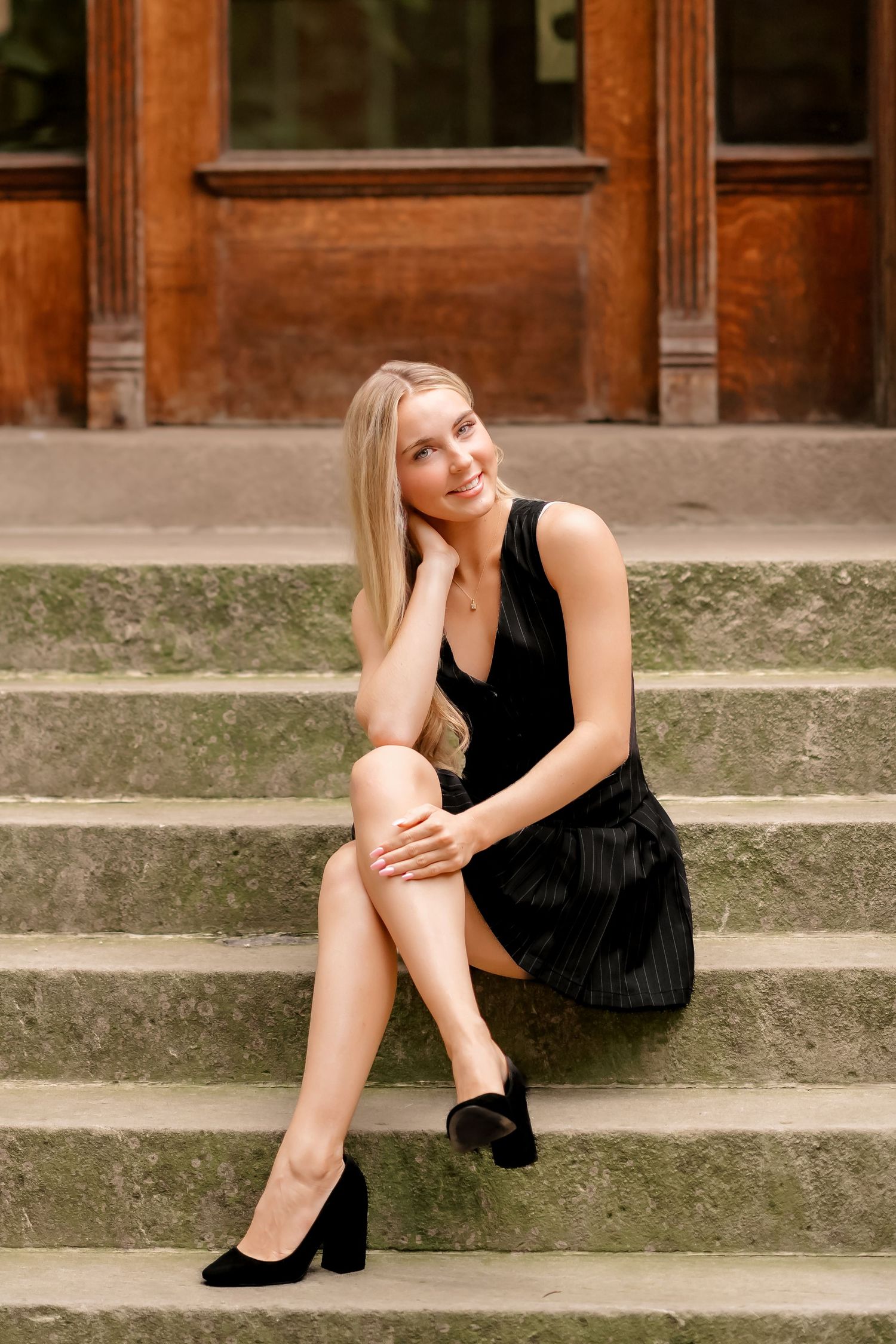 A model in a black dress poses gracefully on concrete steps in an outdoor photoshoot.