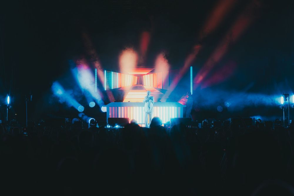 Colorful concert stage lighting illuminates a dark venue with vibrant blue and purple hues creating a dramatic atmosphere.
