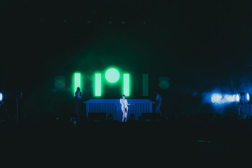 Illuminated green and blue lights create a moody nighttime atmosphere in an urban park setting.