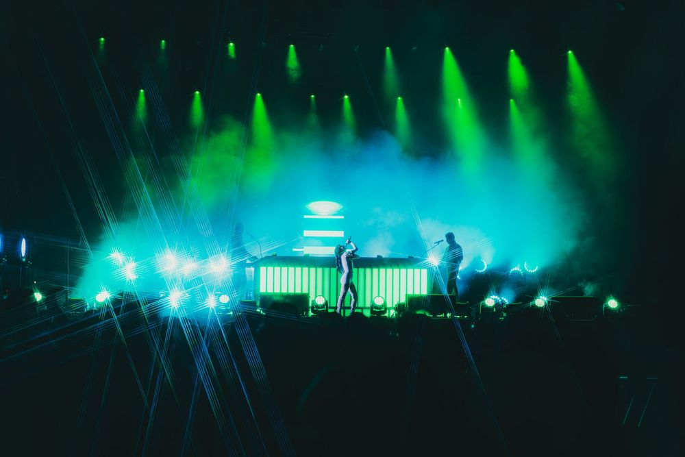 Concert stage illuminated with vibrant green and blue lights creating an atmospheric silhouette during a live performance.