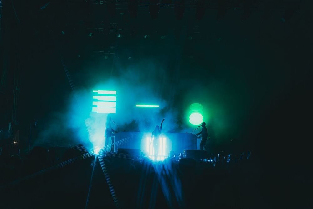 Colorful blue and green stage lights illuminate a dark concert venue creating an atmospheric nightclub ambiance.