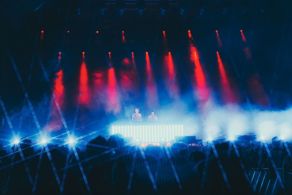 Colorful red and blue lights create a dynamic wave pattern against a dark background in a concert or event setting.