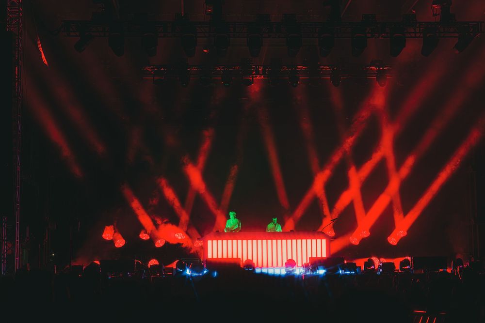 Red laser beams illuminate a dark concert stage with dramatic lighting effects creating an atmospheric performance scene.