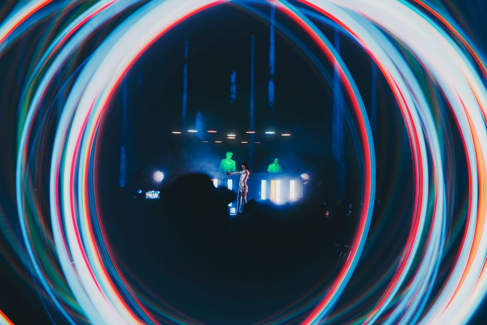 Glowing blue and red neon light trails create circular patterns against a dark background in a long exposure shot.