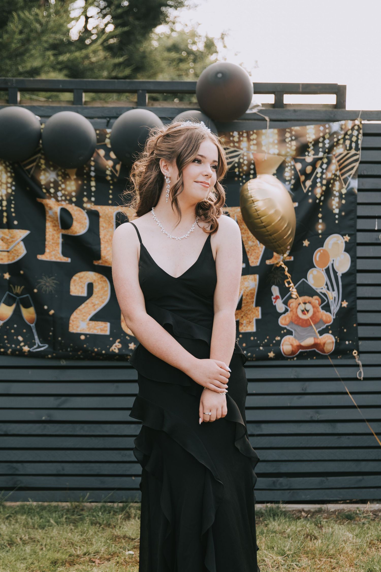 Elegant prom celebration setup with black and gold balloons against dark fence backdrop and decorative lighting.