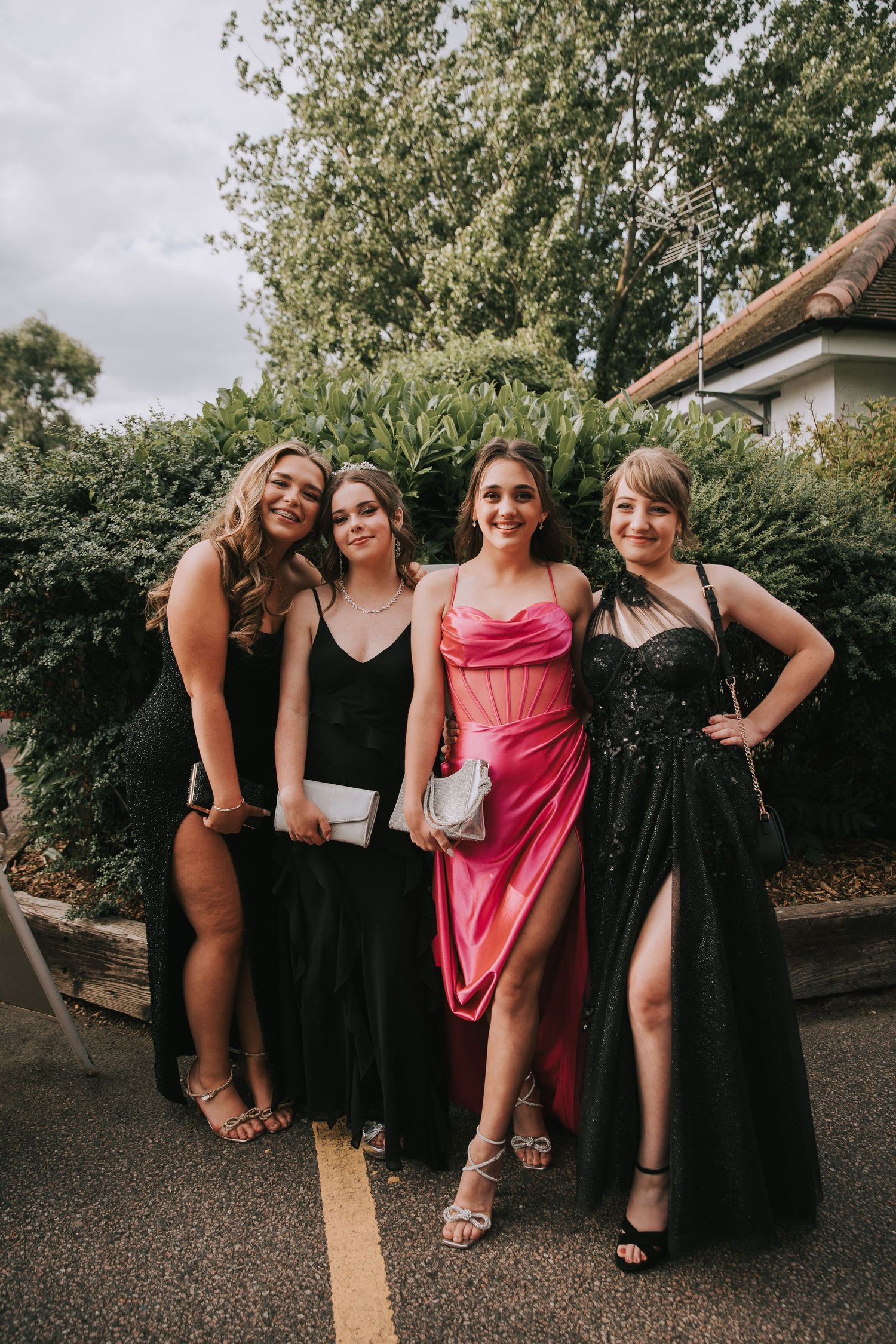 A group of friends pose together outdoors wearing formal evening gowns in black and pink for a special occasion.