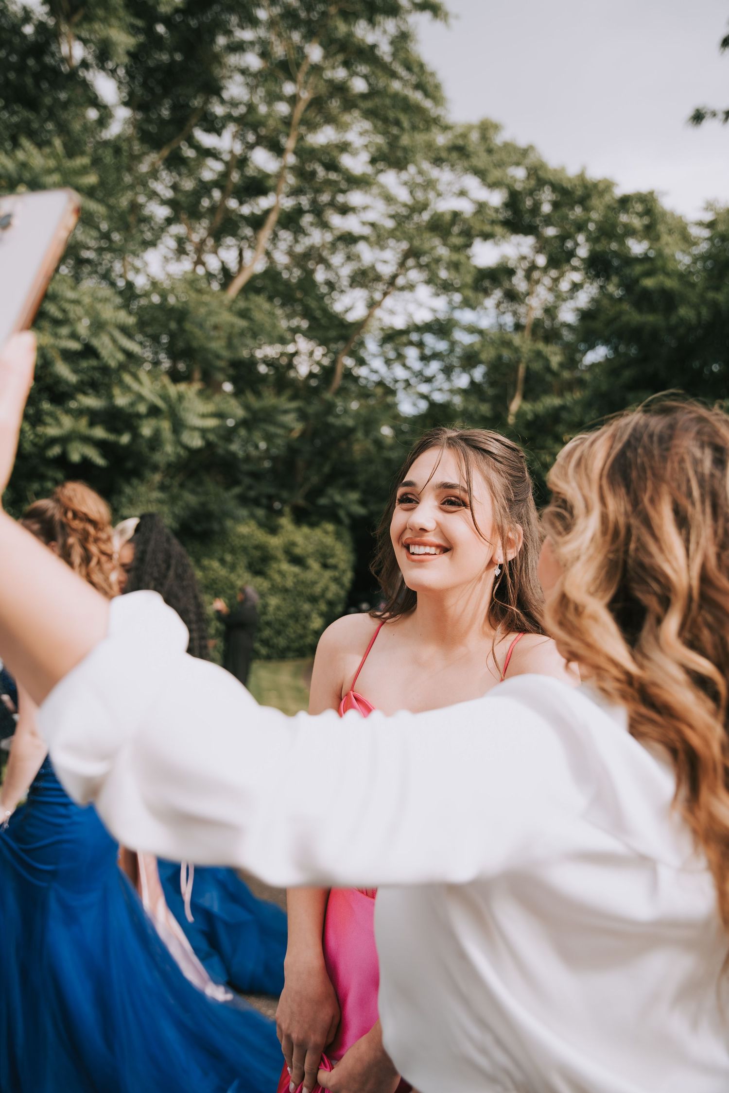 A group of friends in formal attire celebrate together outdoors with trees in the background.