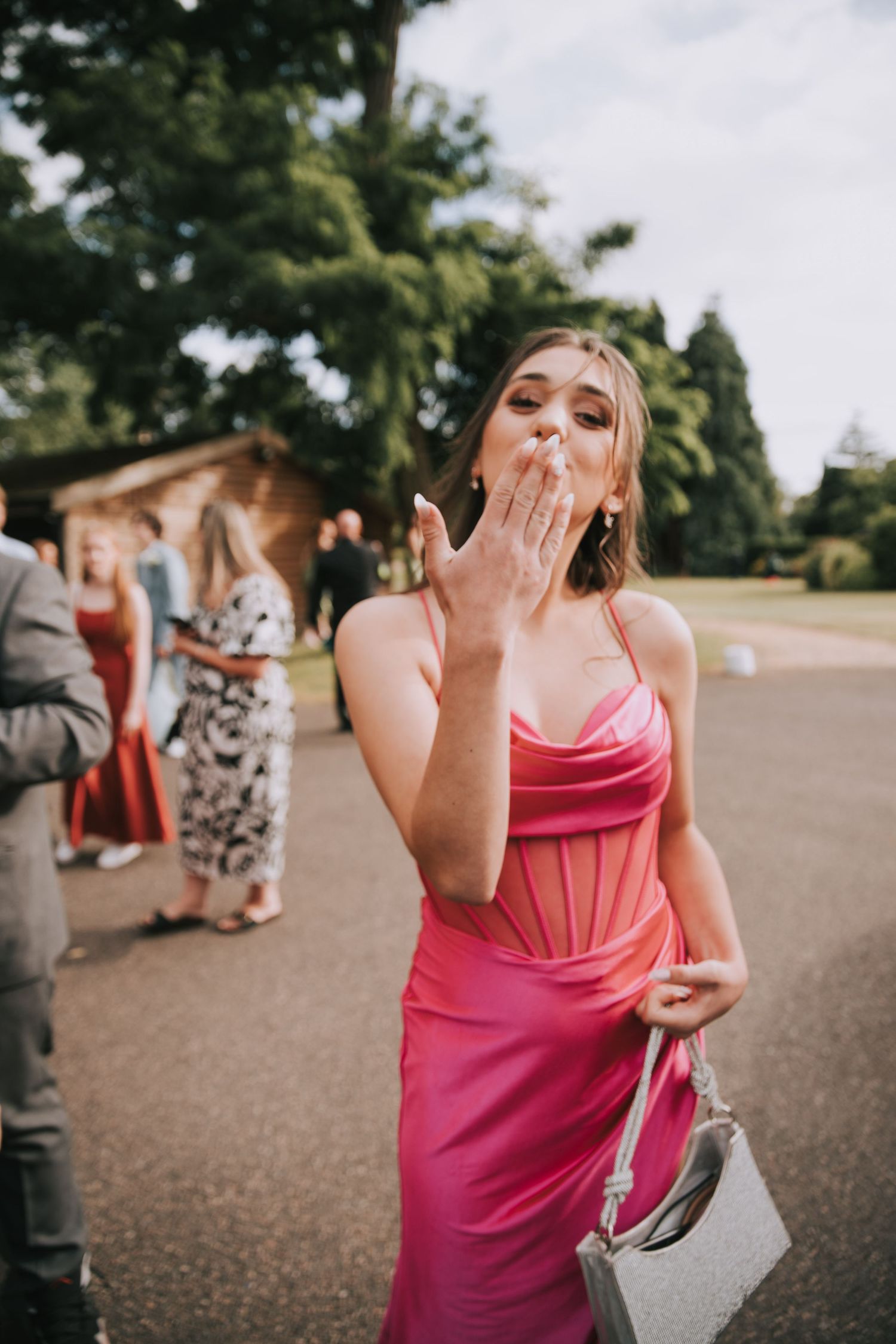 A person in a pink formal dress blows a kiss while standing outdoors at an elegant event.