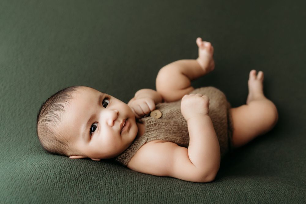 A baby lies on a dark green backdrop in a series of artistic newborn portraits showing different poses and angles.