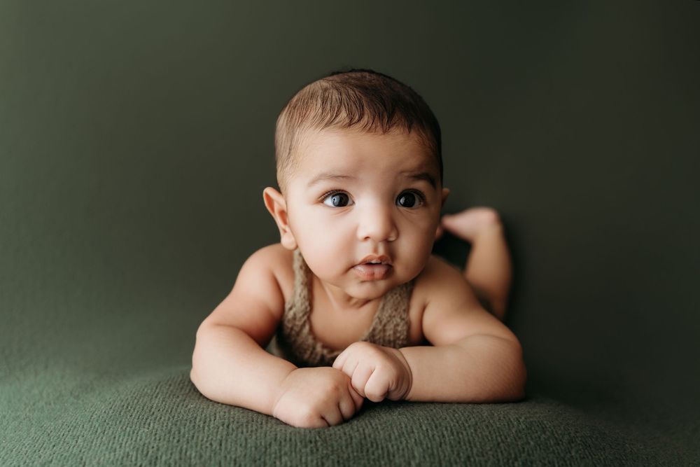A collection of five artistic newborn baby portraits against a dark green studio backdrop.