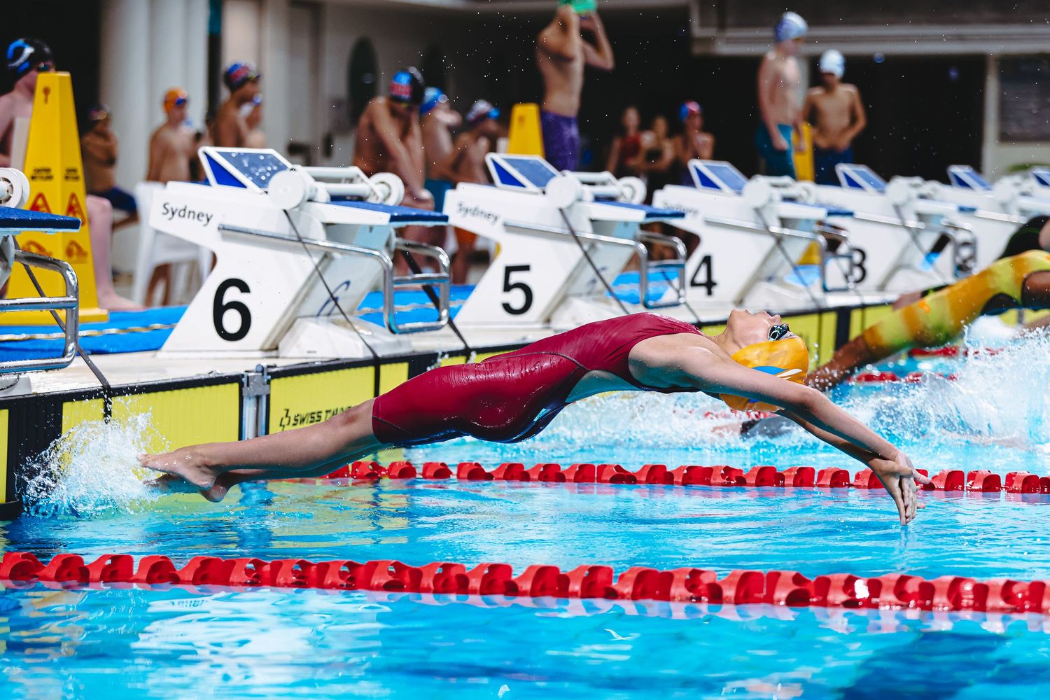 Competitive swimmer performing freestyle stroke in a swimming pool with multiple lane dividers during a race.
