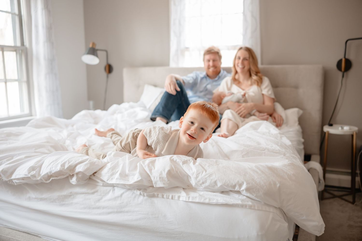 Family lounges together in white bedding during an intimate lifestyle photo session at home.