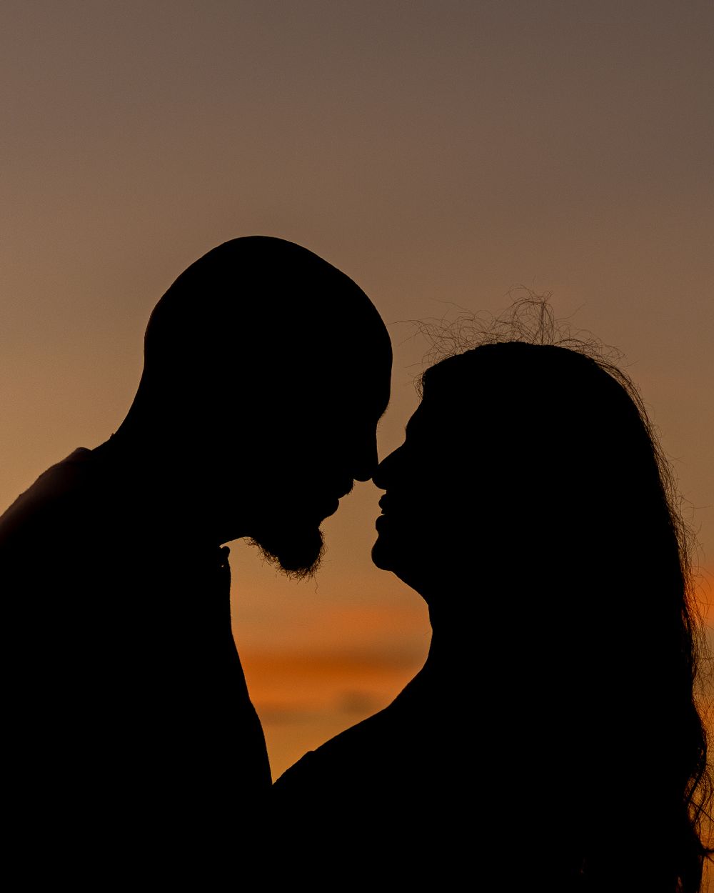 Silhouettes of a romantic couple in profile against a warm sunset sky.