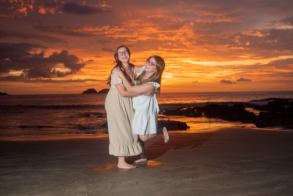 Romantic beach wedding photoshoot silhouettes against vibrant orange sunset sky over ocean waves.