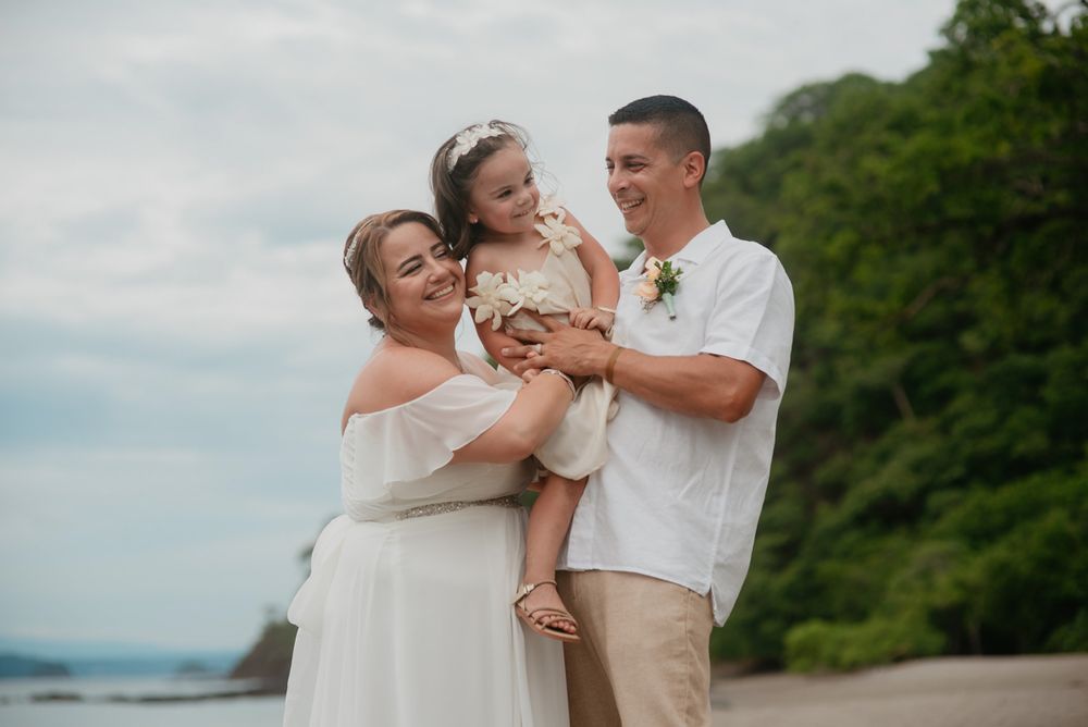 A family shares a joyful moment together on a scenic beach with green hills in the background.