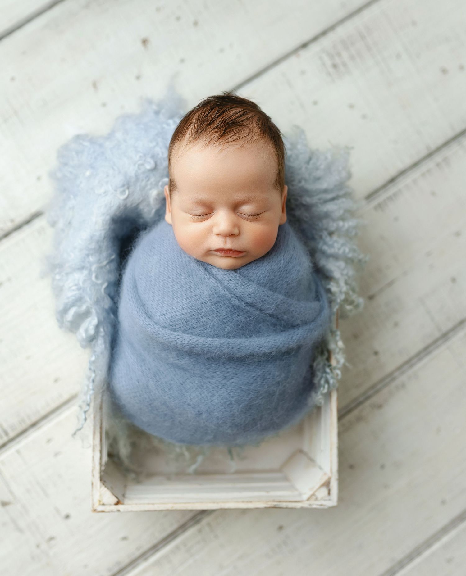 Newborn boy in a blue wrap in a basket with blue fur. - Greenville, SC newborn photographer - Easley, SC newborn photographer.