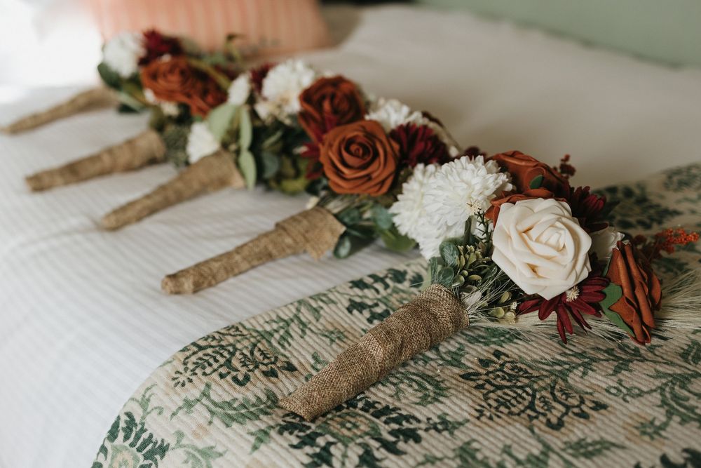 Rustic wedding decorations featuring twine-wrapped utensils adorned with burgundy and cream roses and greenery.