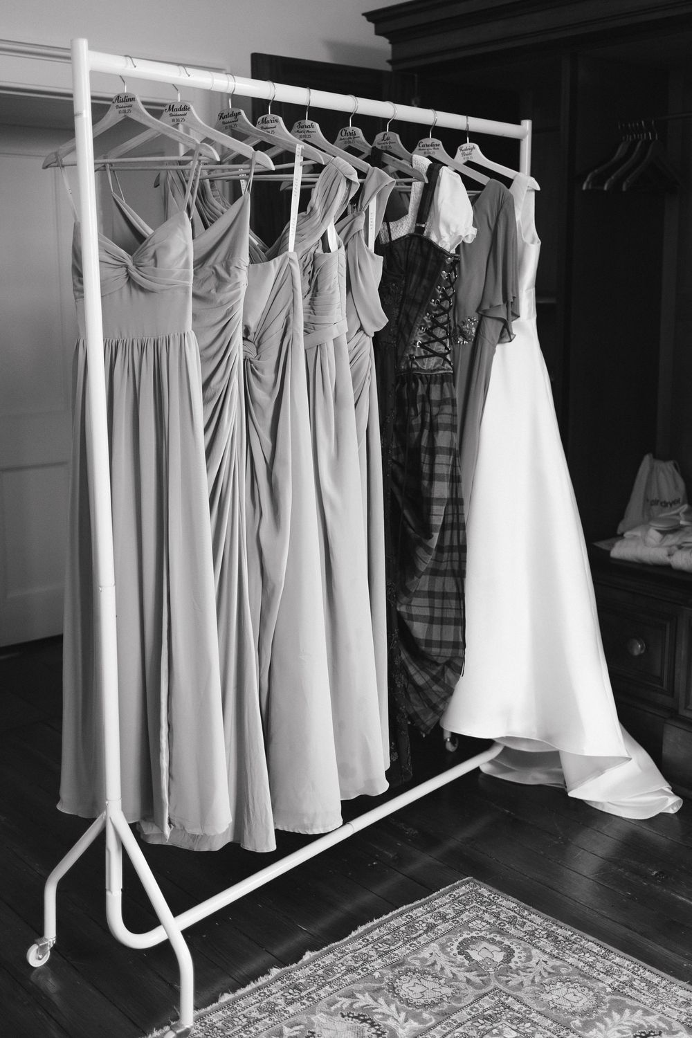 Black and white photograph of elegant wedding dresses hanging on white garment racks in a bridal preparation room.