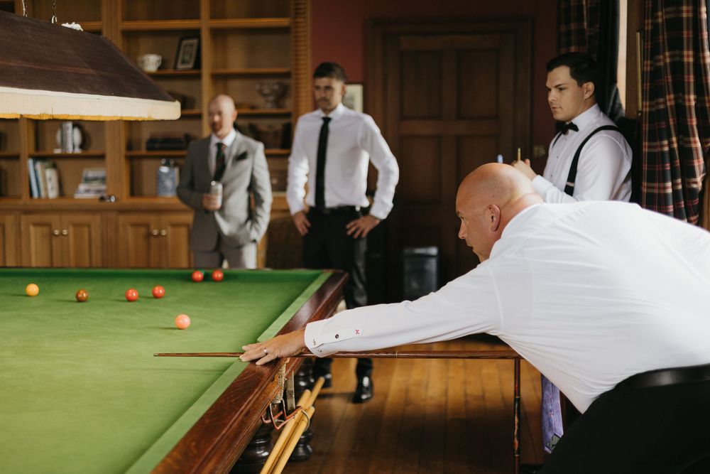 Wide shot of players at a professional snooker tournament in an elegant wood-paneled room.