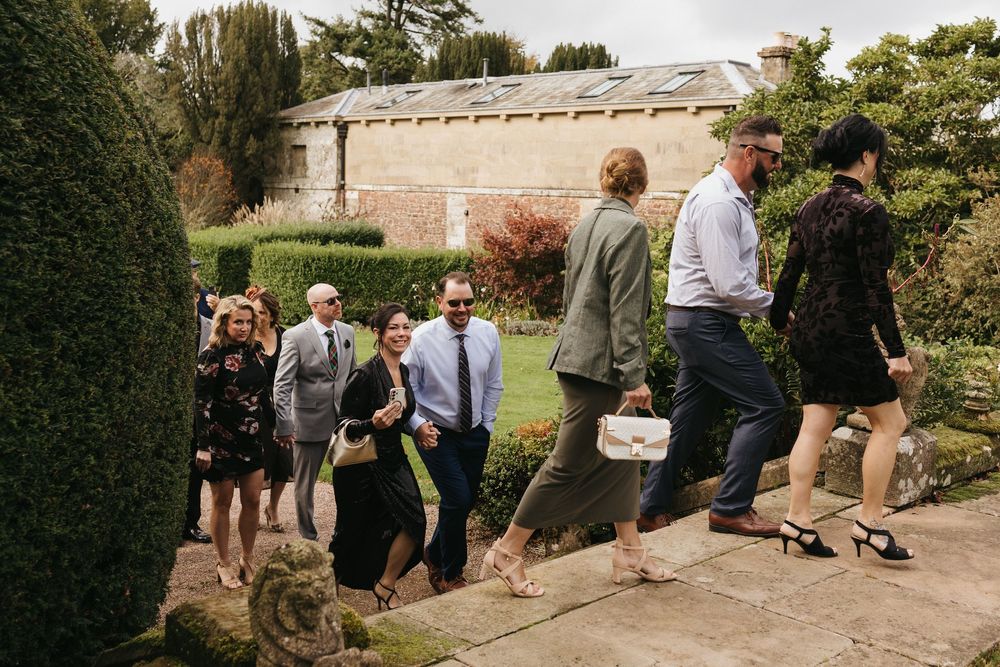A group of guests walk along a stone path beside a garden wall during an outdoor event.