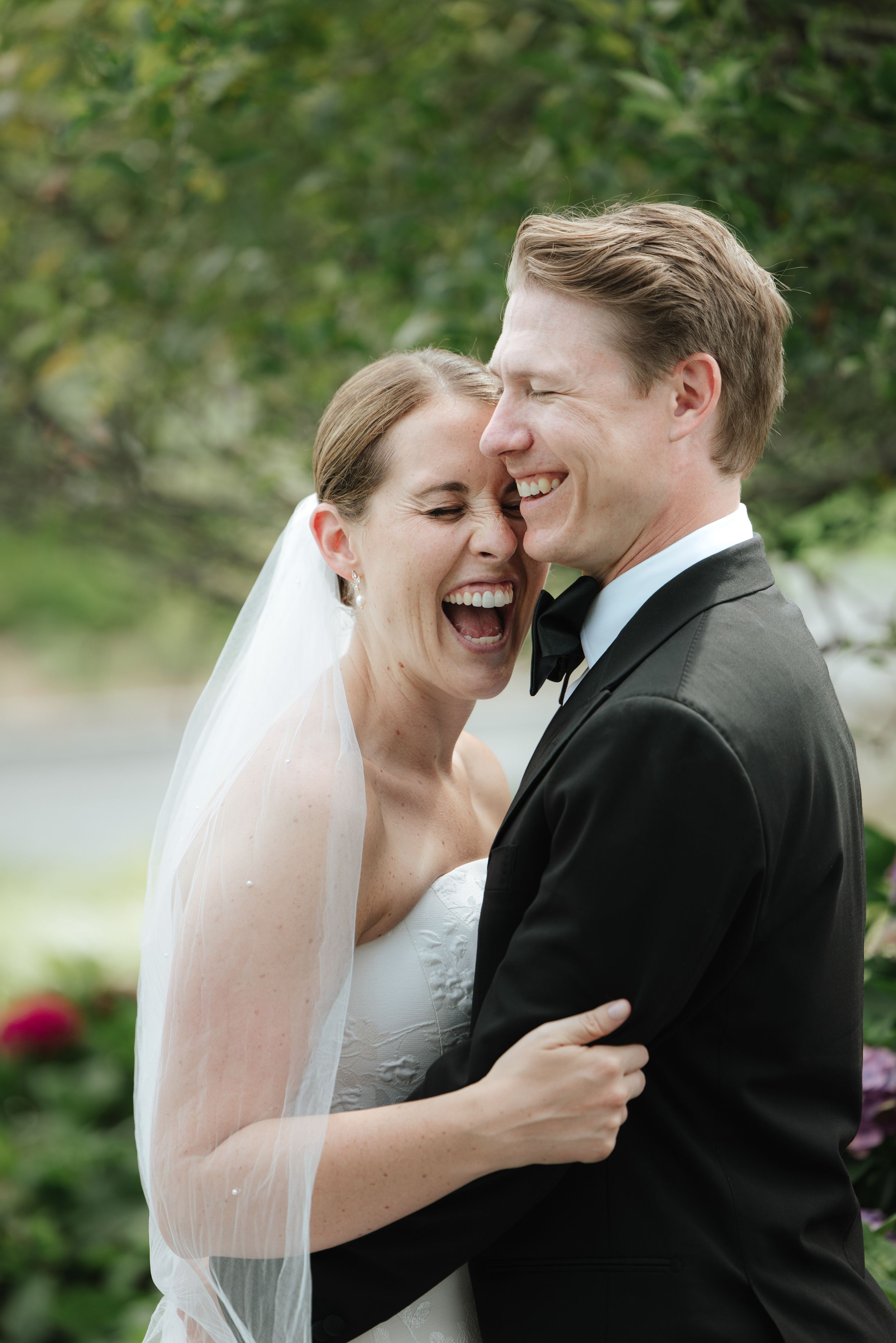 A joyful wedding couple shares an intimate moment of laughter while embracing outdoors.
