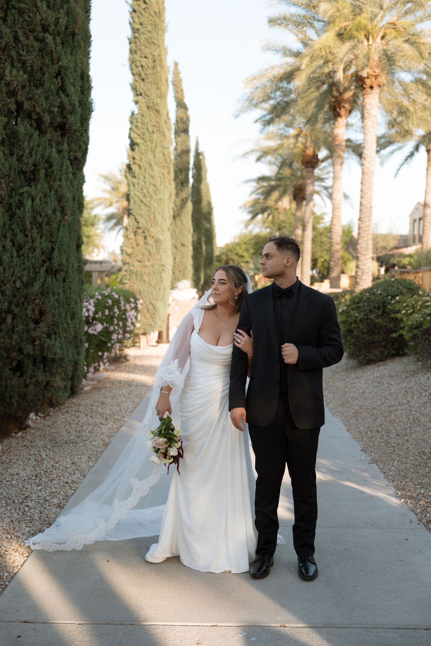 Wedding ceremony guests gather outdoors at dusk under floral archway and string lights for an elegant evening celebration.