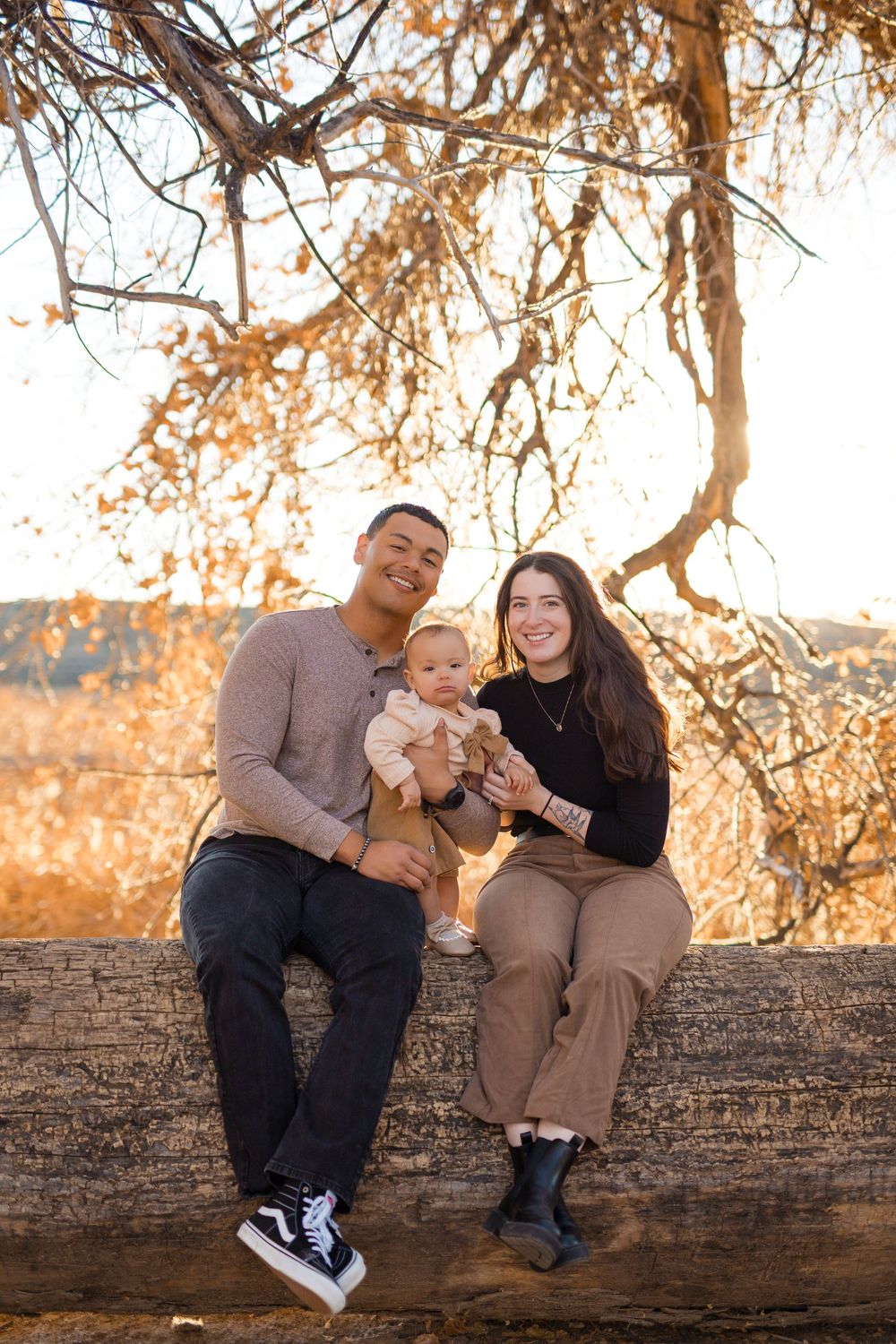 A family sits together on a fallen log during golden hour with autumn trees in the background.