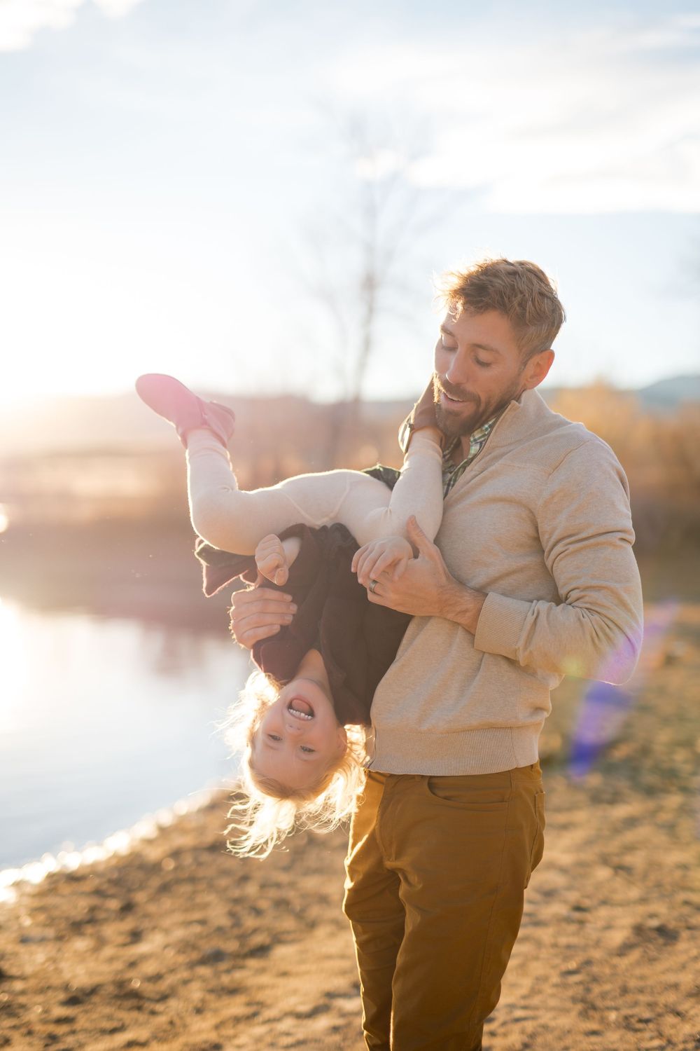 Two people share a joyful moment together on a sandy beach at sunset with golden light streaming through the scene.