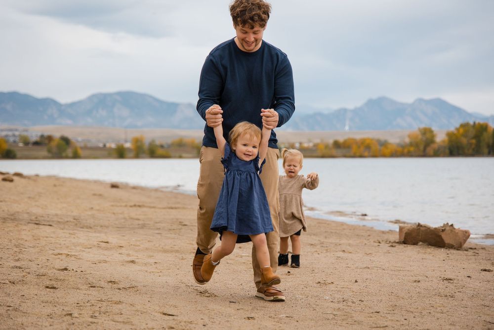 A family walks along a scenic mountain lake shore during autumn with mountains in the background.
