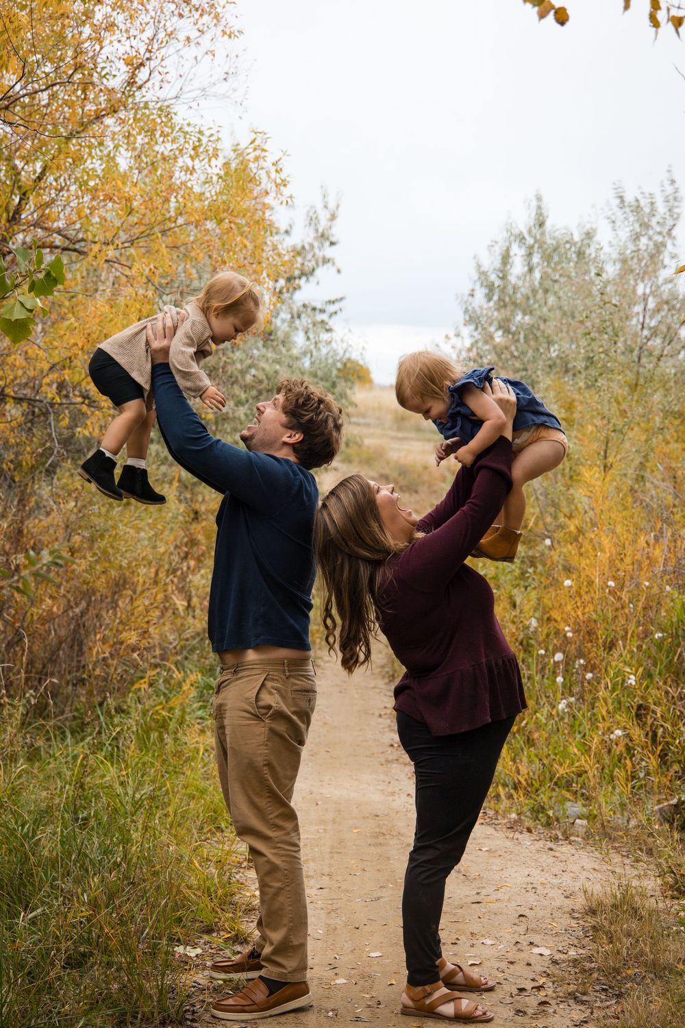 A couple dances playfully on a dirt path surrounded by autumn trees with golden leaves in the background.