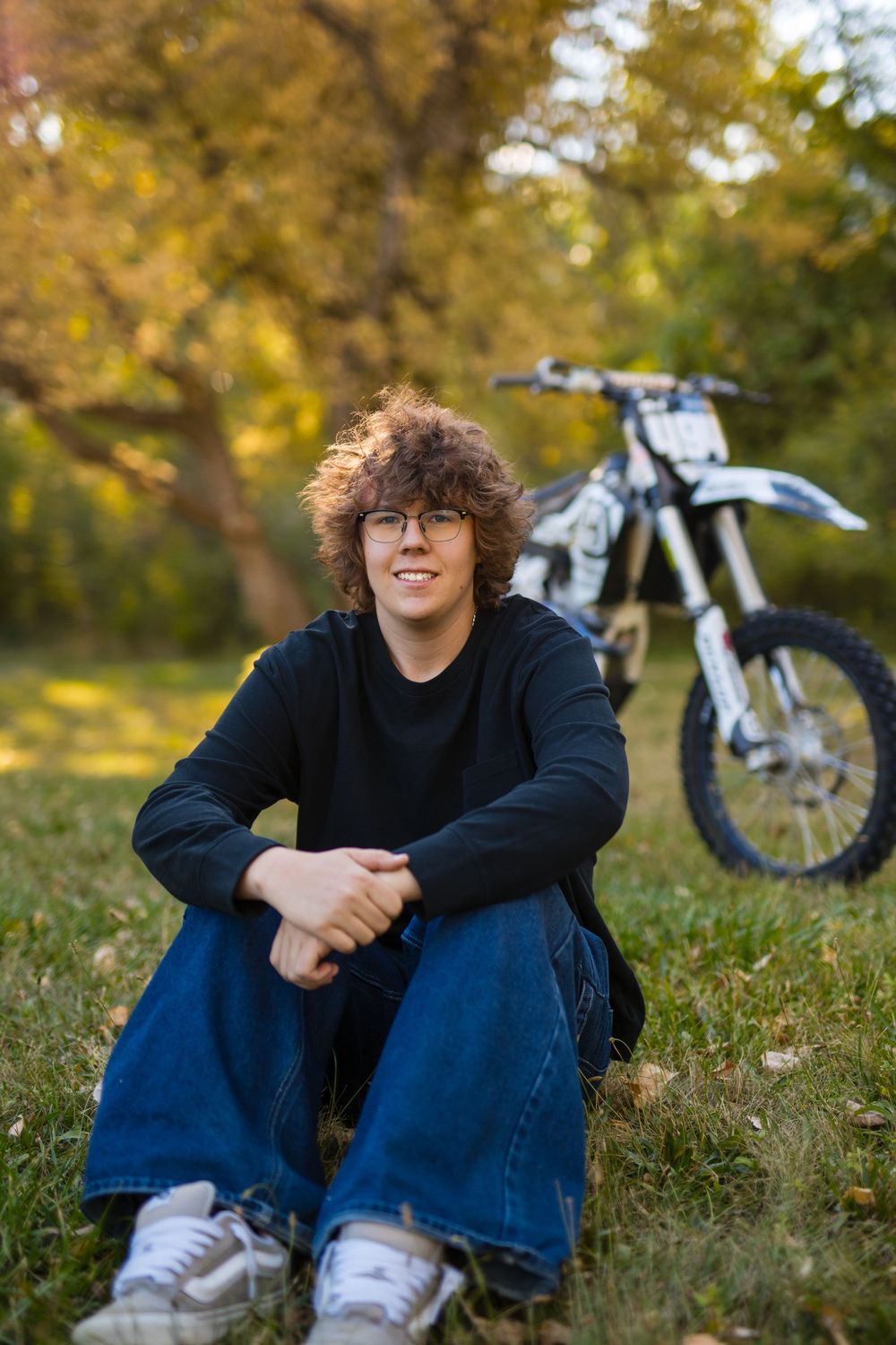 A dirt bike sits in the background of an outdoor autumn scene with golden foliage.