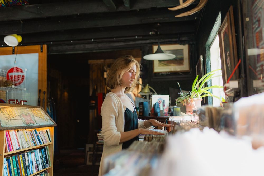 People browse books and gather in a cozy independent bookstore with wooden shelves and warm lighting.