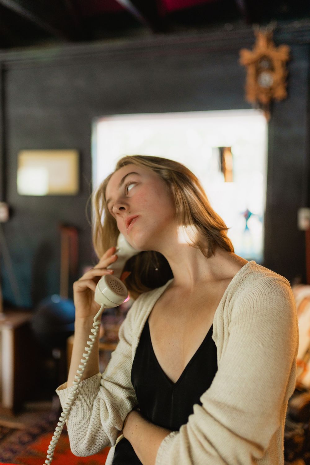 A series of photos showing someone in a cream cardigan and black top talking on a corded telephone in dim lighting.