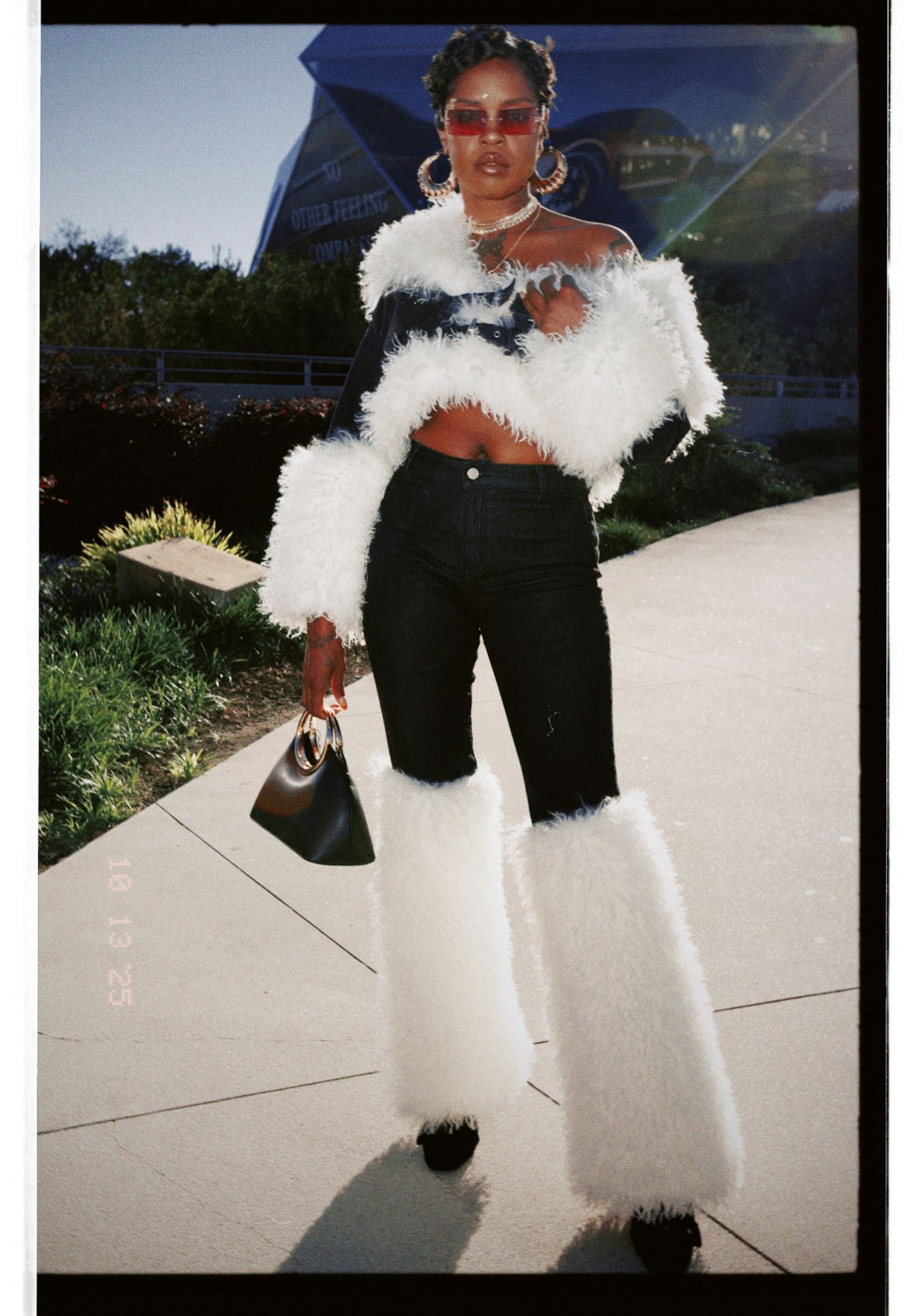 A person wearing a black outfit with white fluffy fur accessories poses in a series of outdoor shots on a sunny day.