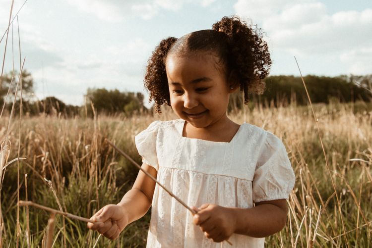 A child in a white dress runs playfully through a golden field at sunset creating a joyful summer scene. Family photoshoot in Manchester.