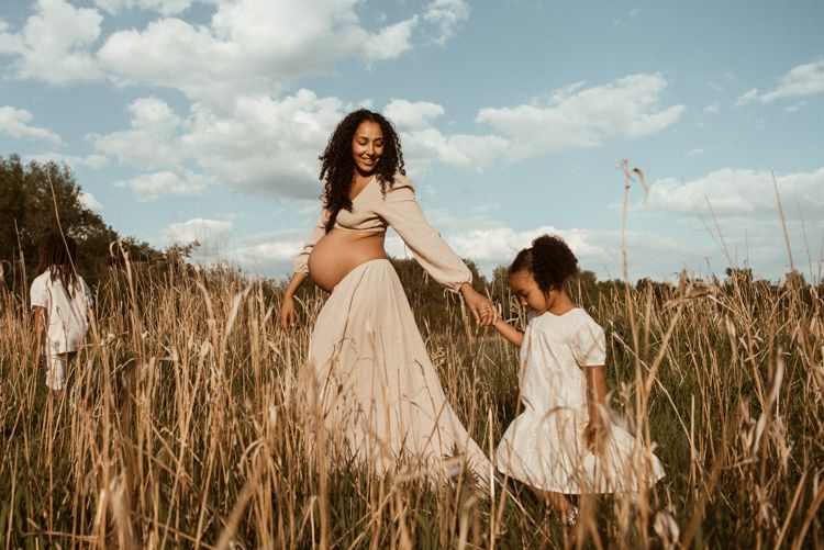 People in flowy white dresses walking through a golden wheat field under a bright blue sky, on a family photoshoot at Fletcher Moss Park.