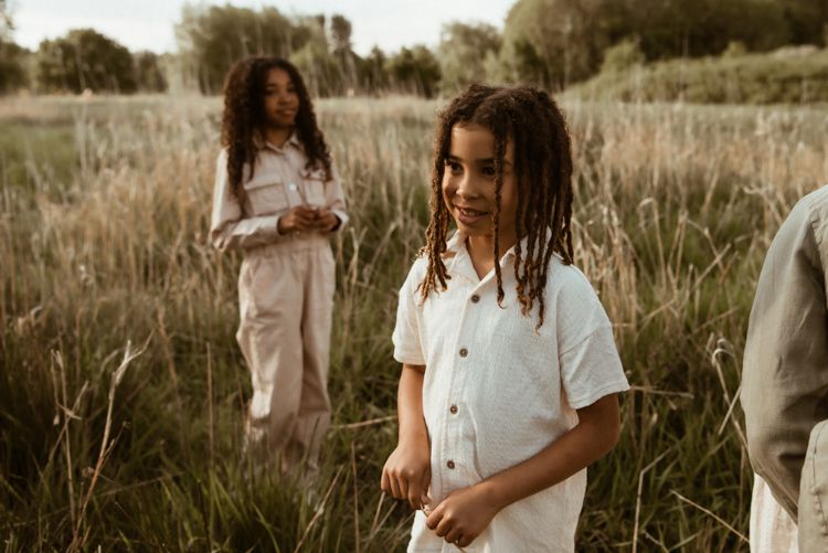 Manchester family photographer captures a couple in white outfits walks through a sunlit field of tall grass during golden hour.