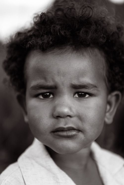 Black and white portrait of a young child with curly hair and an intense expression looking at the camera. Manchester family photography.