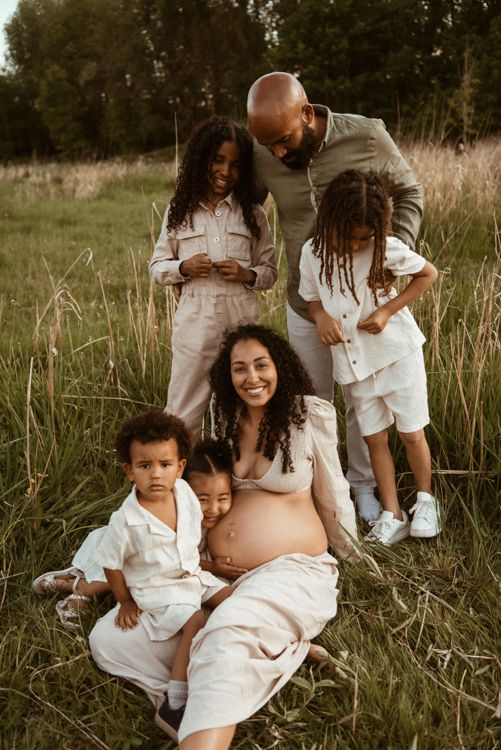 A family in white outfits shares tender moments together while sitting in a grassy field during a golden hour photoshoot in Manchester.