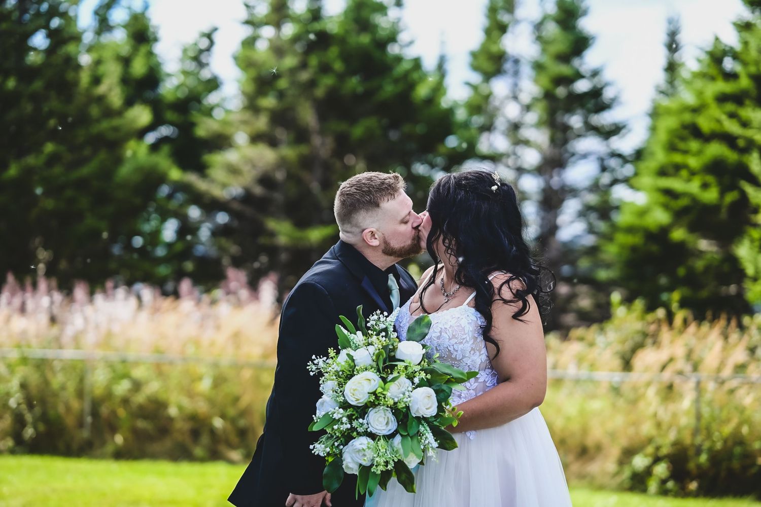 Newlyweds sharing their first kiss in Arnolds Cove, Newfoundland, soft rain and light catching in the air around them.
