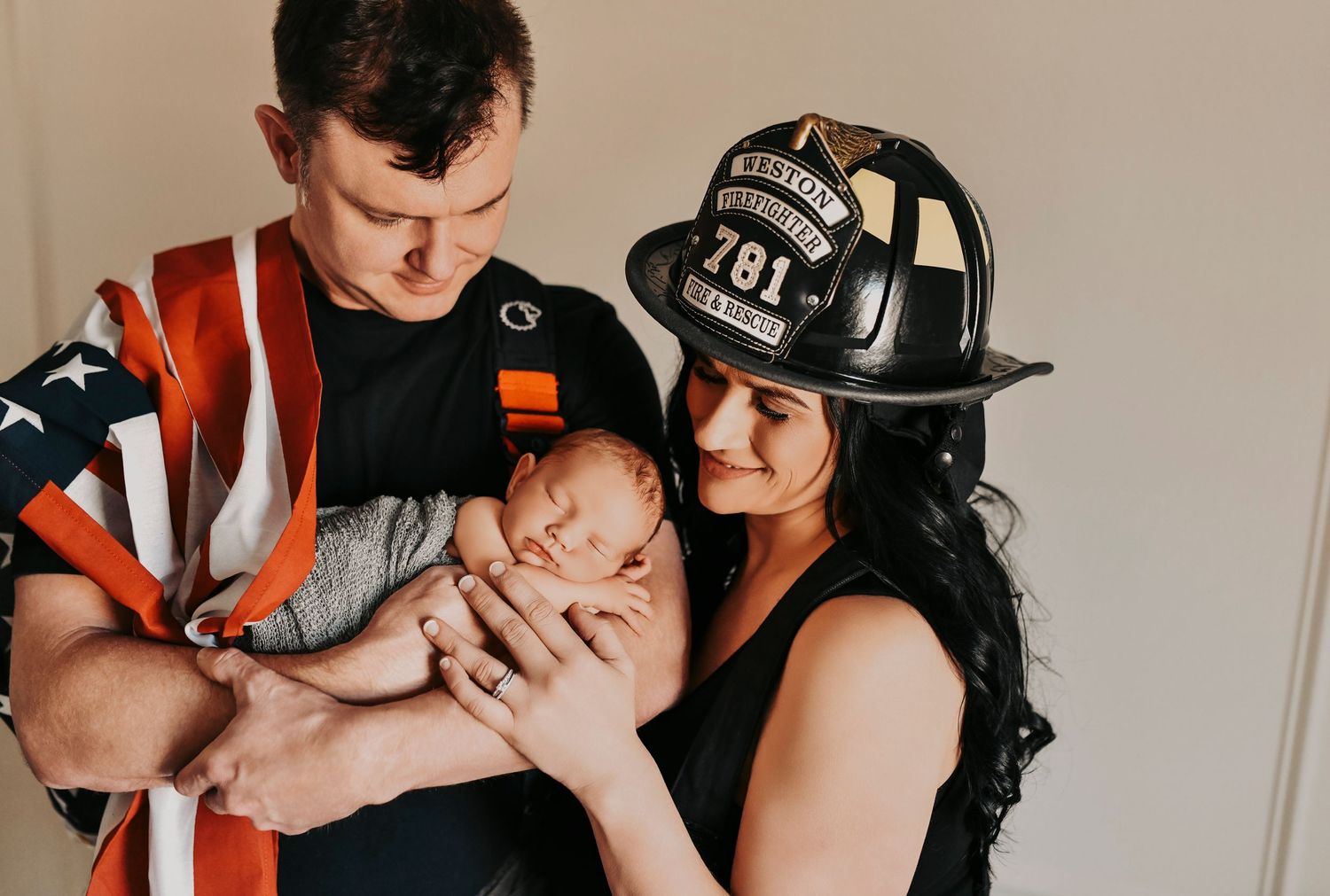 Mother in firefighter gear holding her newborn baby in a timeless, editorial-style newborn session in a Denton Texas studio