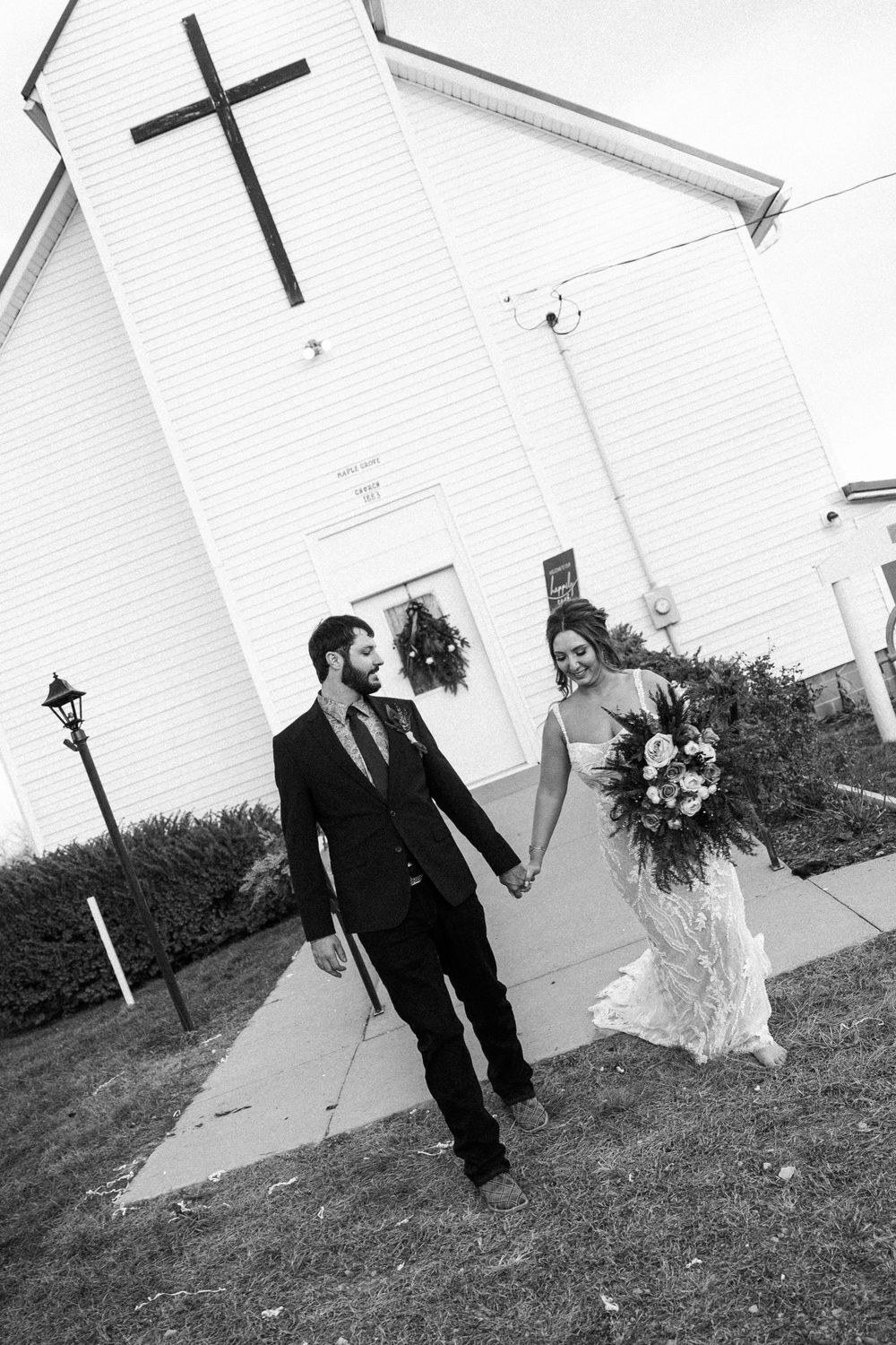 A black and white photo series showing a couple walking and posing in front of a white church building with crosses.