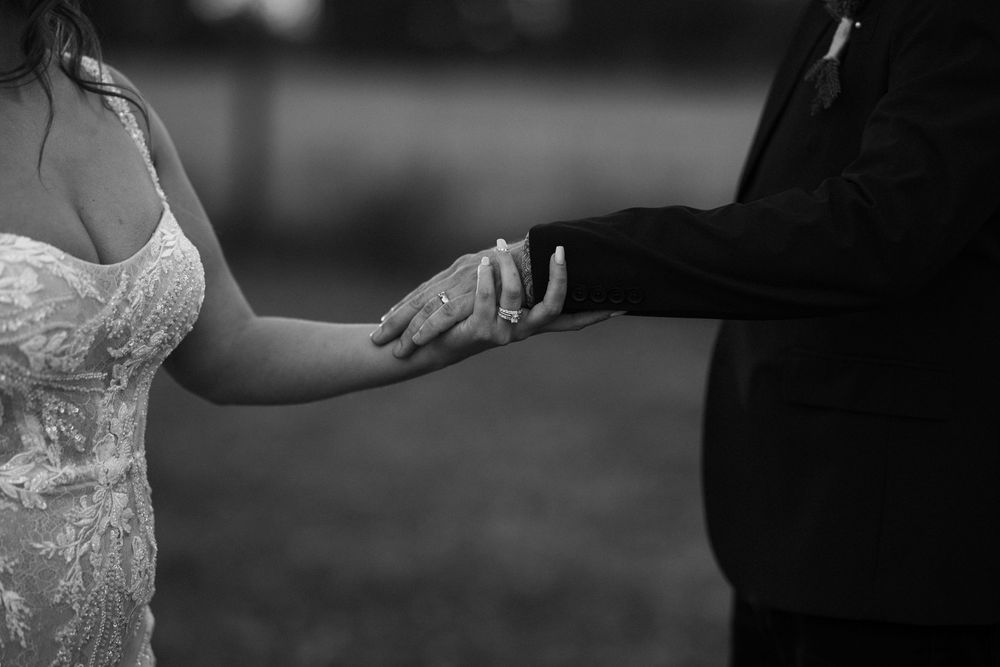 A couple holds hands during an intimate wedding ceremony moment in black and white photography.
