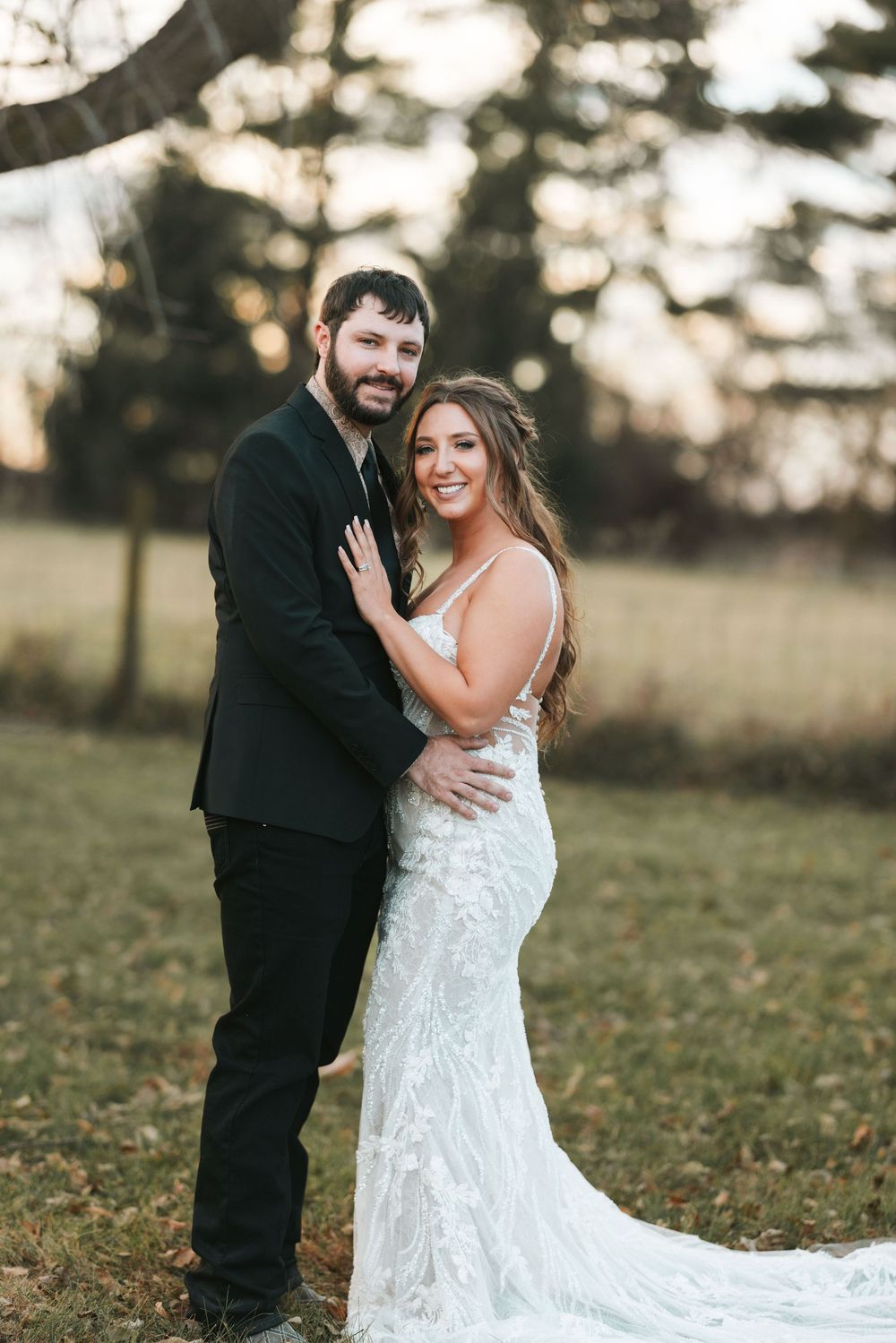 A couple shares romantic moments in an outdoor field setting, with the bride wearing a flowing lace wedding gown.